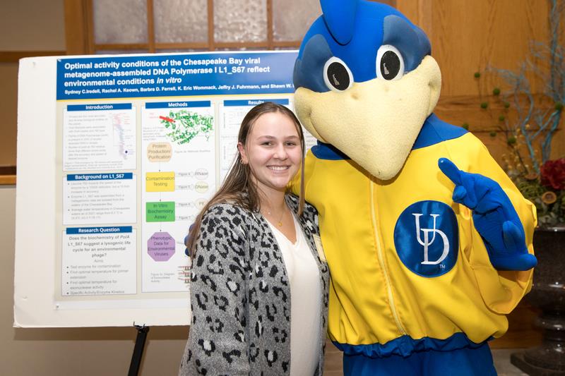 bird mascot and person standing in front of research poster